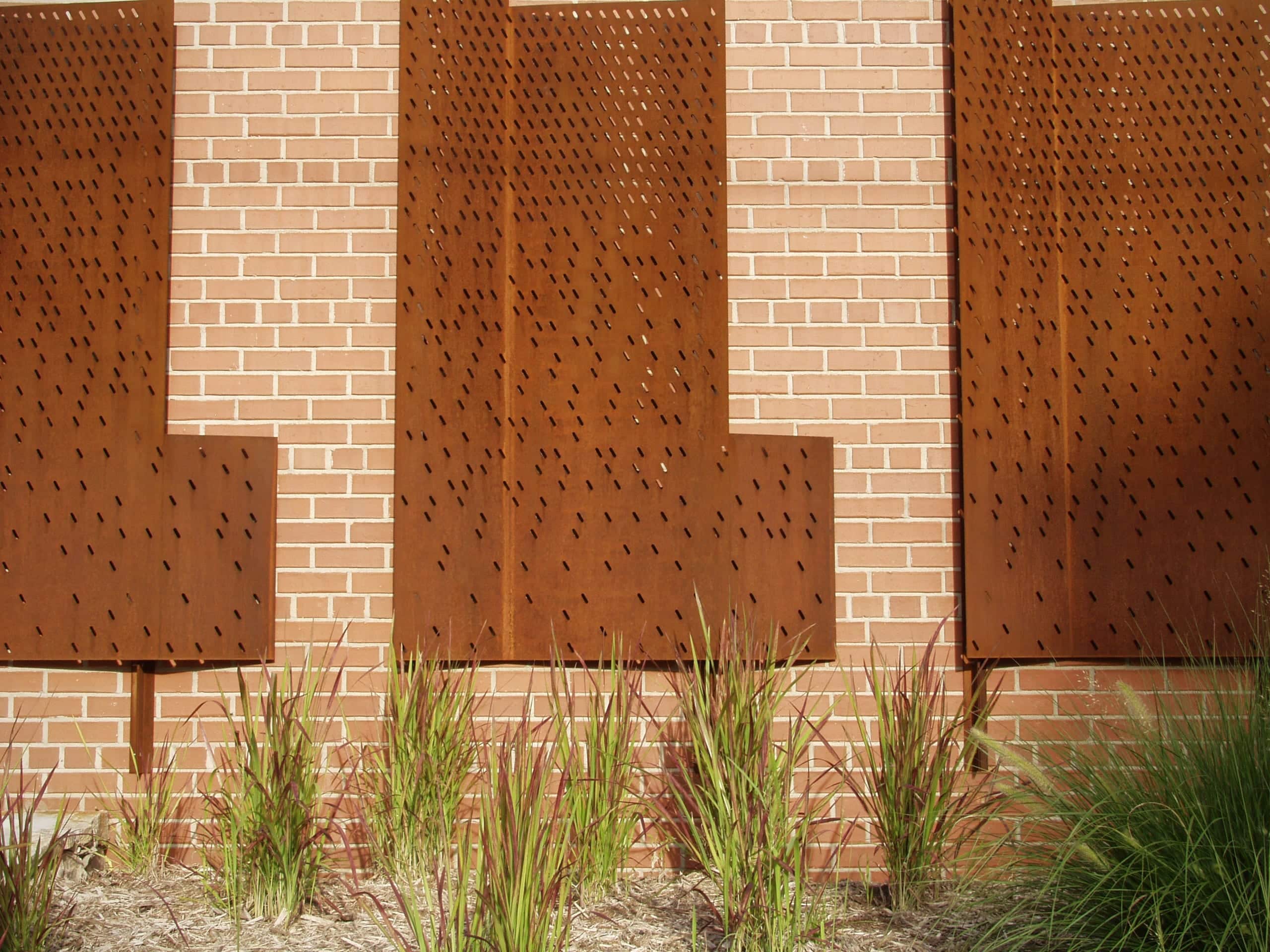 The perforated metal gate motif continues onto the brick wall as an wall-mounted metal artwork.